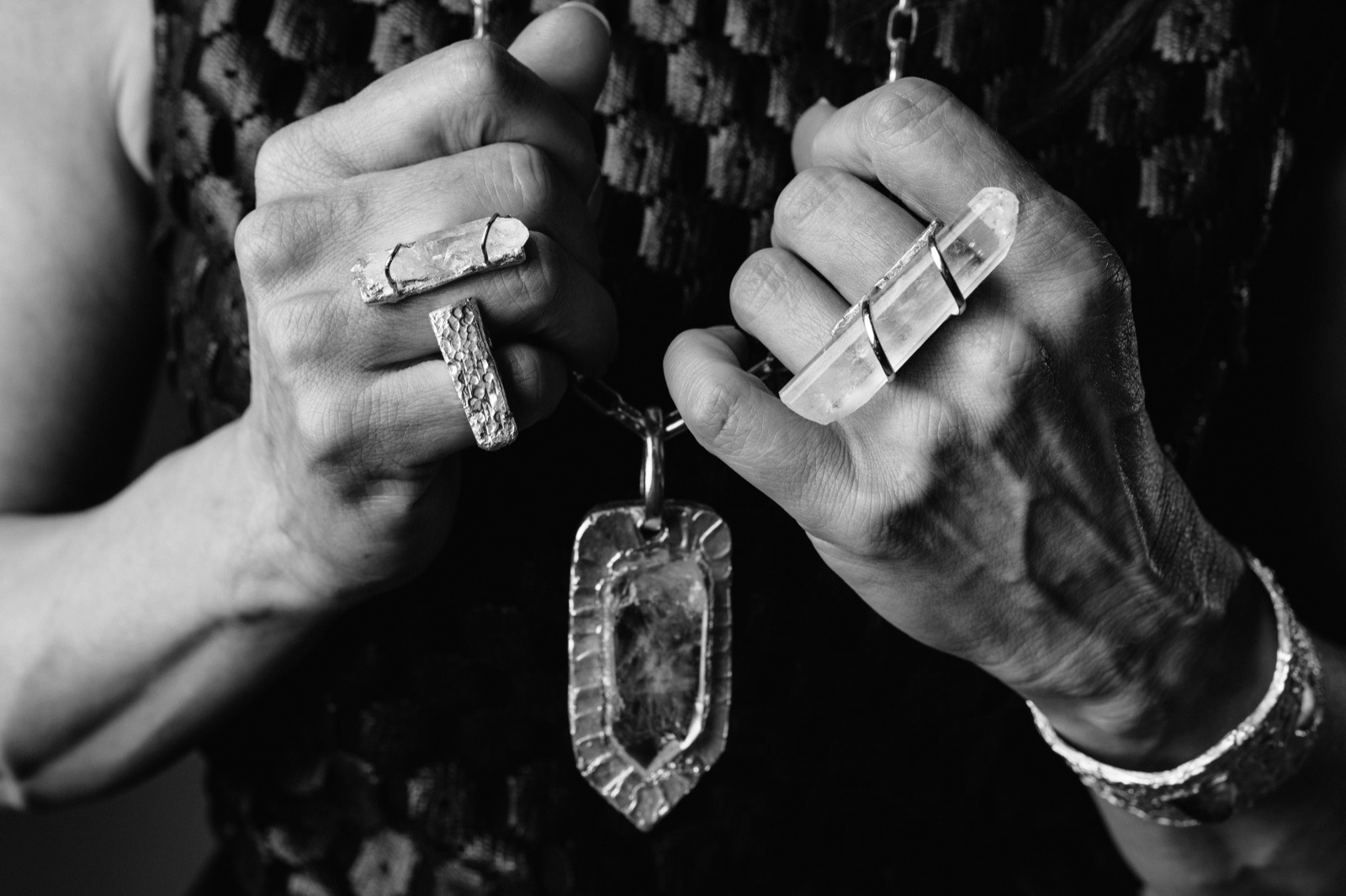 Ana-Lucia's fist wearing silver rings and holding a raw quartz pendant