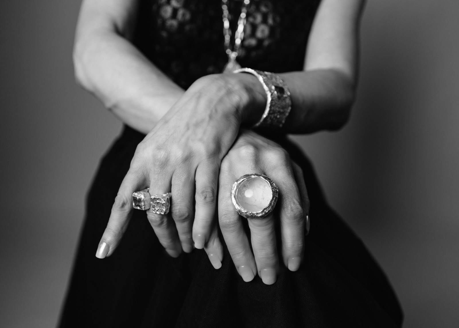 Crossed hands wearing silver rings, a bracelet, and a chain necklace